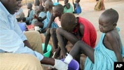 Ajak Kuol Nyamchiek watches while John Lotiki, a nurse with the Carter Center, bandages blisters on her leg from where a guinea worm is emerging, Abuyong, Sudan, Nov. 4, 2010.