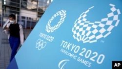 A woman walks near a sing of the Tokyo 2020 Olympic and Paralympic Games, Aug. 20, 2021, in Tokyo.