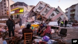 Warga duduk dan berdiri di sekitar reruntuhan bangunan yang hancur akibat gempa di Golbasi, provinsi Adiyaman, selatan Turki, 8 Februari 2023. 