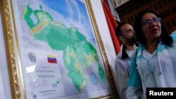 Dos personas conversan cerca de un mapa enmarcado de Venezuela, promovido por el gobierno de Nicolás Maduro para anexar un nuevo estado, el Guayana Esequiba, en Caracas, el 8 de diciembre de 2023.