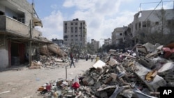 Palestinci prolaze pored zgrada uništenih u izraelskim zračnim napadima u kampu Nuseirat u središnjem pojasu Gaze, ponedjeljak, 16. oktobra 2023. (AP Photo/Hatem Moussa)