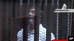 FILE: In this image taken from Egypt State TV, Mohammed Morsi stands inside a glass-encased metal cage in a courtroom in Cairo, Jan. 28. 2014. 