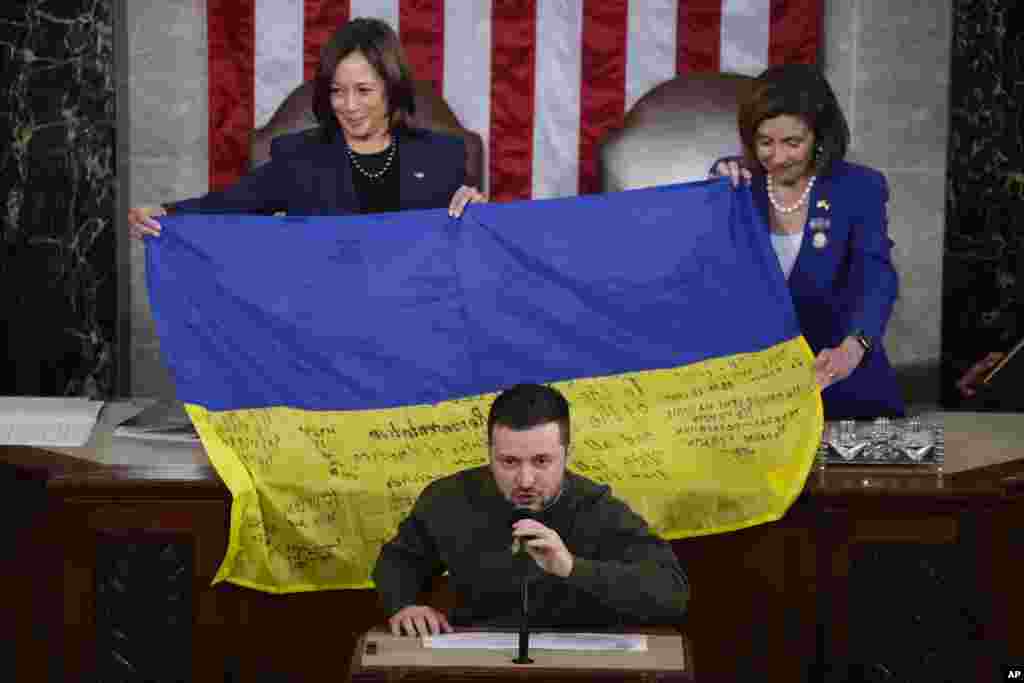 U.S. Vice President Kamala Harris and House Speaker Nancy Pelosi of Calif., right, react as Ukrainian President Volodymyr Zelenskyy presents lawmakers with a Ukrainian flag autographed by front-line troops in Bakhmut, in Ukraine's contested Donetsk province, as he addresses a joint meeting of Congress on Capitol Hill in Washington, Dec. 21, 2022.