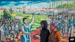 A couple wearing face masks walk past a painting to mark the country's Youth Day holiday in Soweto, South Africa, June 16, 2020. 