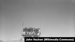 A 1940 photograph of a signpost at Wounded Knee. Sacred Heart Catholic Church, in the background, burned down during the 1973 AIM takeover.