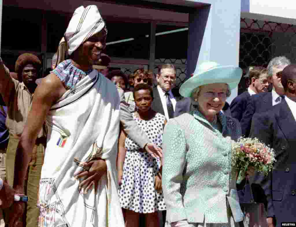Britain's Queen Elizabeth II, accompanied by Port Elizabeth mayor Nceba Faku, in Xhosa traditional dress, smile at residents outside the Centenary hall in New Brighton township, March 22, 1995. The Queen is on a six-day official visit to South Africa, her first to the country since 1947.