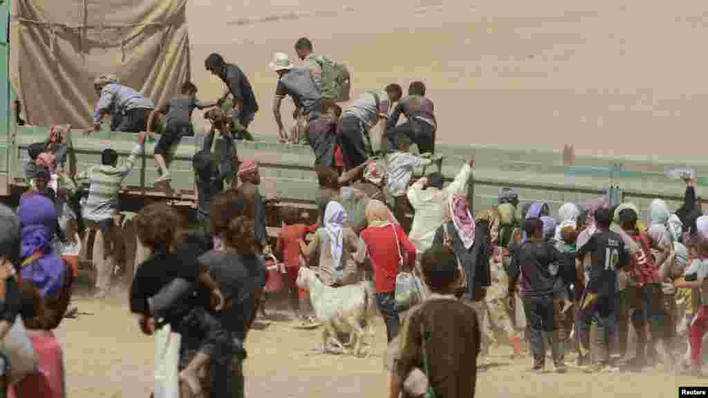 Displaced people from the minority Yazidi sect jump onto a truck as they make their way toward the Syrian border town of Elierbeh of Al-Hasakah Governorate, Aug. 10, 2014.