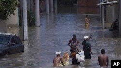 Un grupo de personas camina en medio de una calle inundada tras fuertes lluvias en Duque de Caxias, Brasil, el lunes 15 de enero de 2024. 