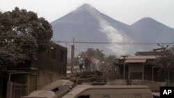 Tim penyelamat berjalan di atas atap di kawasan Escuintla, Guatemala, Senin, 4 Juni 2018, yang diselimuti abu vulkanik tebal yang dimuntahkan oleh Volcan de Fuego (Gunung Api Api) yang nampak di belakangnya. 