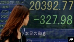 一位女士走过东京一家证券公司显示显示日经指数下跌的电子屏幕。（2015年8月12日）