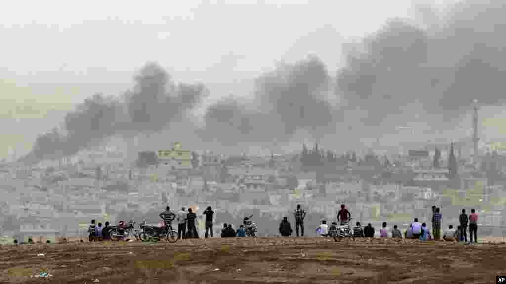 People on a hilltop watch smoke rising from a fire caused by a strike in Kobani, Syria, during fighting between Syrian Kurds and the militants of Islamic State group, on the outskirts of Suruc, at the Turkey-Syria border, Oct. 11, 2014.