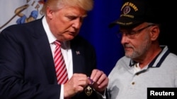 Donald Trump conversa con el Coronel Louis Dorfman, quien le regaló una medalla Corazón Púrpura, en la escuela Briar Woods High School de Ashburn, Virginia.