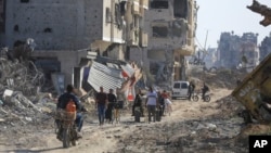 Palestinos caminan entre la destrucción dejada por la campaña aérea y terrestre israelí en Jan Yunis, en el sur de la Franja de Gaza, el domingo 7 de abril de 2024.