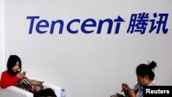 FILE - Visitors use their smartphones underneath the logo of Tencent at the Global Mobile Internet Conference in Beijing, May 6, 2014. 