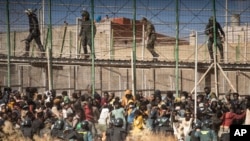 Polisi anti huru-hara memasang pengaman ketika para migran tiba di wilayah Spanyol setelah menyeberangi pagar yang memisahkan kantong Spanyol dan Maroko di Melilla, Spanyol, Jumat, 24 Juni 2022. (Foto: AP Photo/Javier Bernardo)