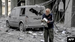 Seorang pria Palestina membaca buku di depan sebuah mobil yang rusak akibat serangan udara Israel di Kota Gaza, 3 Maret 2024. (Foto: AFP)