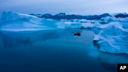 A boat navigates at night between icebergs in eastern Greenland, late Aug. 15, 2019.