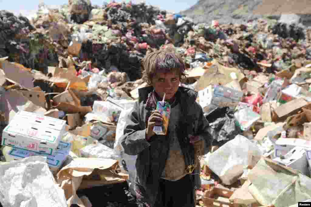 Seorang anak laki-laki minum air jus yang sudah kadaluwarsa di tumpukan sampah di pinggiran Sana'a, Yaman.