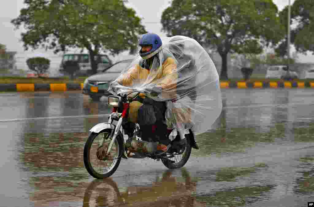 A motorcyclist and passenger cover themselves with plastic sheet to protect from rain at a highway, in Islamabad, Pakistan.