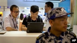 FILE - In this April 29, 2015 file photo, visitors use a laptop computer at a display booth as a security guard stands nearby at the Global Mobile Internet Conference in Beijing. A coalition of international business groups has appealed to China in a letter dated Wednesday, Aug. 10, 2016 to change proposed cybersecurity rules they warn will harm trade and isolate the country.