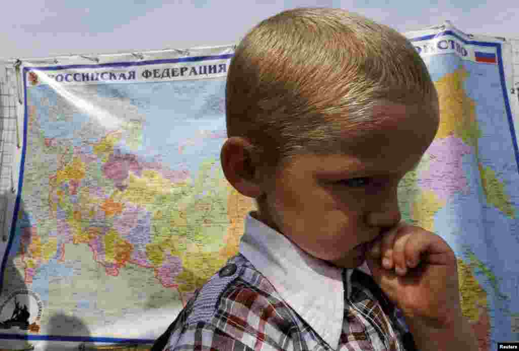 A boy stands in front of a map of Russia at a refugee camp set up for Ukrainian refugees, outside Donetsk, Aug. 18, 2014. 
