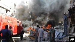 Warga berkumpul di sekitar gedung yang terbakar pasca ledakan bom di daerah sub-urban Sayyida Zaenab, Damaskus, Suriah (11/6). 