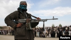 FILE - A member of the Taliban insurgent and other people stand at the site during the execution of three men in Ghazni Province, Afghanistan, April 18, 2015. 
