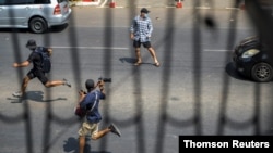 Pro-democracy protesters and a journalist run as riot police officers advance them during a rally against the military coup in Yangon, Myanmar, Feb. 27, 2021.