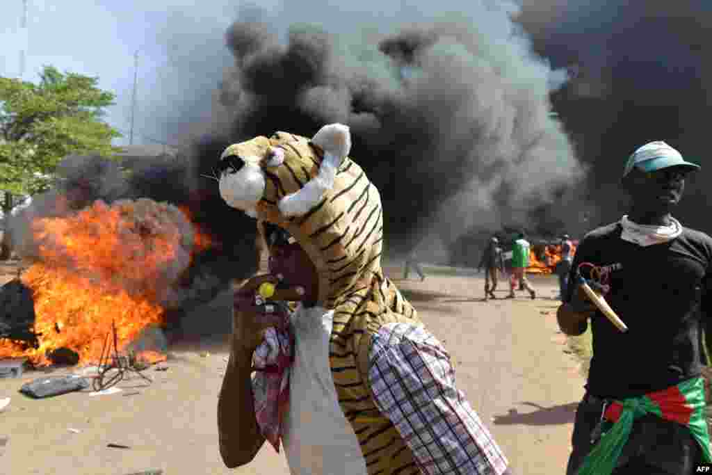 Para demonstran berdiri di luar gedung parlemen saat terjadinya pembakaran mobil-mobil dan dokumen di Ouagadougou, Burkina Faso (30/10).