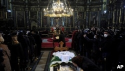A woman kisses a protective screen over the coffin of Patriarch Irinej as he lies in repose at the Congregational church in Belgrade, Serbia, Nov. 21, 2020.