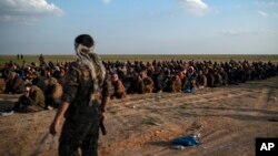 FILE - In this Feb. 22, 2019 file photo, U.S.-backed Syrian Democratic Forces (SDF) fighters stand guard next to men waiting to be screened after being evacuated out of the last territory held by Islamic State group militants, near Baghouz, eastern…