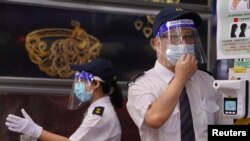 FILE - Security guards wearing face shields and masks check shoopers' body temperatures at an entrance of a shopping center in Hong Kong, Aug. 11, 2020.