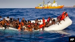 Migrants ask for help from a dinghy boat as they are approached by the SOS Meditrranee's ship Aquarius, background, off the coast of the Italian island of Lampedusa, April 17, 2016.
