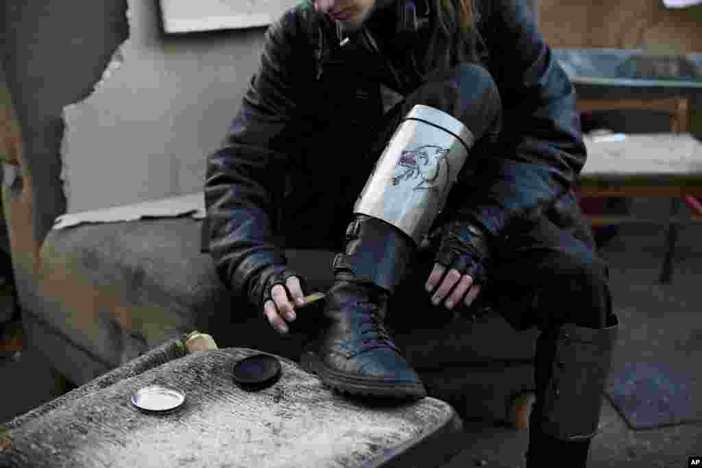 Seorang anggota kelompok relawan pertahanan diri, dengan pelindung tulang kering darurat bergambarkan serigala, menyemir sepatu boots miliknya di Lapangan Kemerdekaan Kyiv, Ukraina, 11 Maret 2014. 