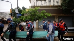 Los remeros preolímpicos brasileños Evaldo Mathias Becker y Piedro Tuchtenhagen y otros llevan un barco utilizado para rescatar a las víctimas de las inundaciones en Porto Alegre, estado de Rio Grande do Sul, Brasil, 10 de mayo de 2024.