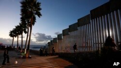 People walk along the U.S. border wall in an oceanside park in Tijuana, Mexico, at sunset, Nov. 30, 2018.