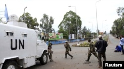 Polisi wa Mombasa wapita mbele ya watu wanaosimama nyuma ya eneo la usalama mbele ya kanisa ambalo washambuliaji waliwafyetulia risasi waumini, Likoni Mombasa, March 23, 2014. 