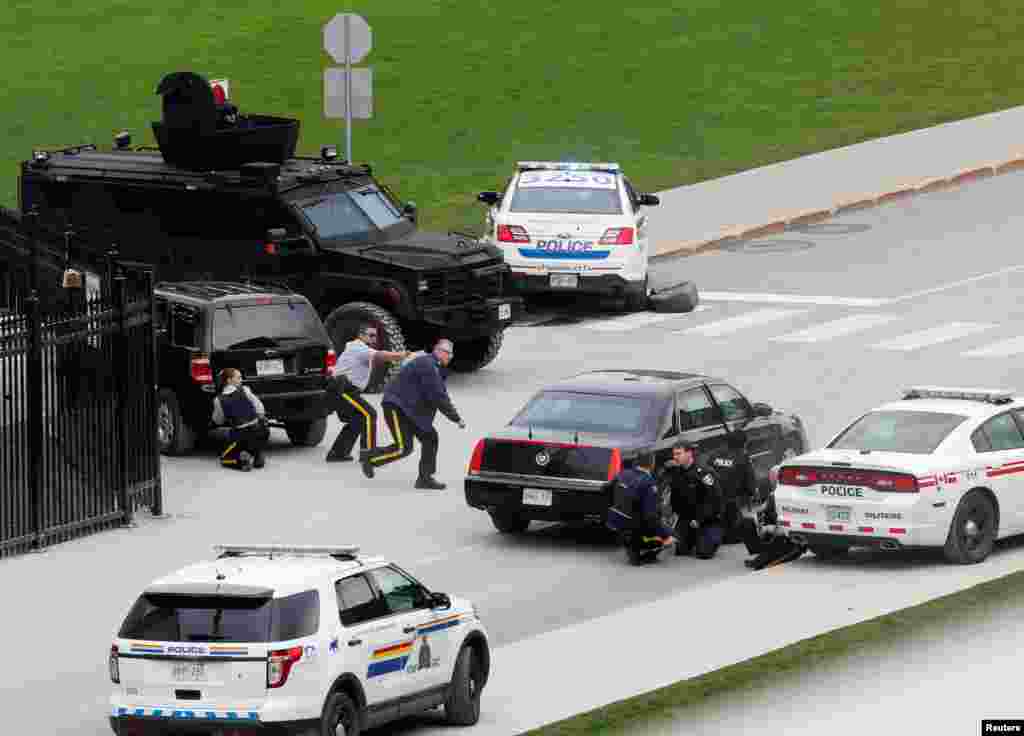 Police officers take cover near Parliament Hill following a shooting incident in Ottawa.