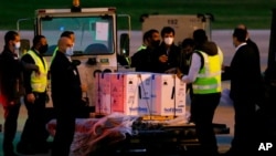 Para pekerja berdiri di samping kotak-kotak pengiriman pertama vaksin COVID-19 buatan Pfizer-BioNTech yang tiba di Bandara Internasional Rafik Hariri di Beirut, Lebanon, Sabtu, 13 Februari 2021. 