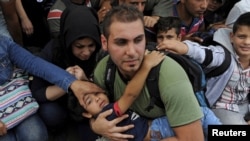FILE - A man holds a boy as refugees and migrants wait to cross the borders of Greece with Macedonia, near the village of Idomeni, Sept. 6, 2015. 