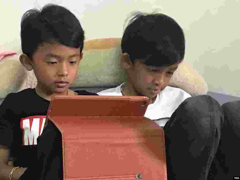Kem Vesnamano and Kem Vesnamane are seen watching videos on their iPad tablets, July 2, 2017. (Sok Khemara/VOA Khmer)