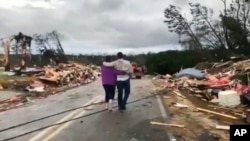 Warga berjalan di antara puing-puing yang berserakan pasca dihantam tornado di Lee County, Alabama, Minggu, 3 Maret 2019.