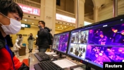 A staff member wearing a mask monitors thermal scanners that detect temperatures of passengers at the security check inside the Hankou Railway Station in Wuhan, China, Jan. 21, 2020.