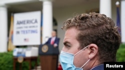 Seorang anggota staf Presiden Donald Trump mengenakan masker wajah di Rose Garden saat Trump memberikan keterangan pers tentang Covid-19 di Gedung Putih, Wasington, 11 Mei 2020.