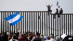 Central American migrants sit on top of the border wall on the beach in San Diego during a gathering of migrants living on both sides of the border, April 29, 2018. 