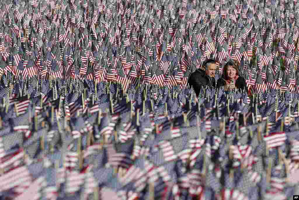 Sepasang warga Amerika memotret diri mereka sendiri di antara lautan bendera di sebuah pelataran di Boston, 26 Mei 2013. Bendera tersebut dipajang untuk mengenang warga Massachusetts yang gugur dalam perang, sejak Perang Saudara hingga saat ini, dengan dukungan dana dari "Massachusetts Military Heroes Fund". (AP Photo / Michael Dwyer)