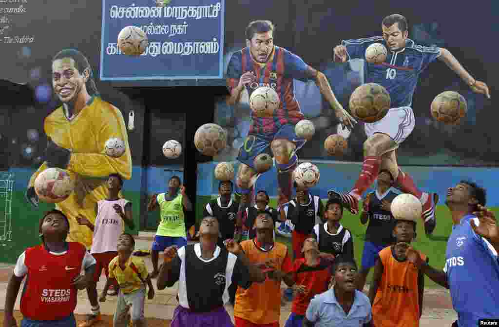 Boys practice during a heading drill in front of murals of (L-R), Brazil's Ronaldinho, Argentina's Lionel Messi and France's Zinedine Zidane, at a playground in the southern Indian city of Chennai.