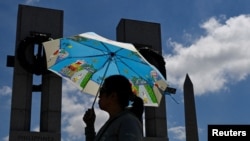 Seorang pengunjung Monumen Peringatan Perang Dunia II di Washington tampak memakai payung untuk berlindung dari sengatan matahari di tengah gelombang panas yang melanda Washington, pada 19 Juni 2024. (Foto: Reuters/Craig Hudson)