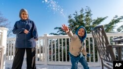 Omar Abu Kuwaik throws snow shortly after arriving from Gaza at the residence of the Global Medical Relief Fund as Khaolah Obahi of Rahma Worldwide looks on, Wednesday, Jan. 17, 2024. (AP Photo/Peter K. Afriyie)