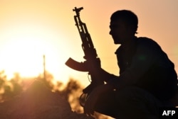FILE - A fighter from the Kurdish People's Protection Units (YPG) poses for a photo at sunset in the Syrian town of Ain Issi, some 50 kilometers north of Raqqa, during clashes between IS group jihadists and YPG fighters, July 10, 2015.